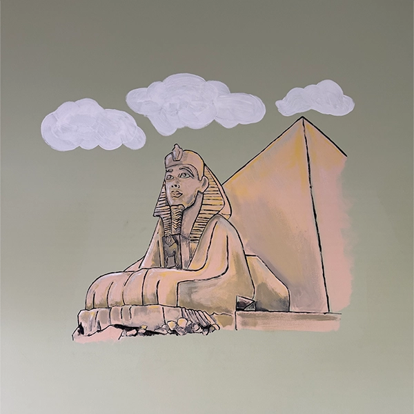 A mural depicting a sphinx seated before a pyramid, set against a pastel green background with soft, white clouds above. A mural depicting a sphinx seated before a pyramid, set against a pastel green background with soft, white clouds above.
